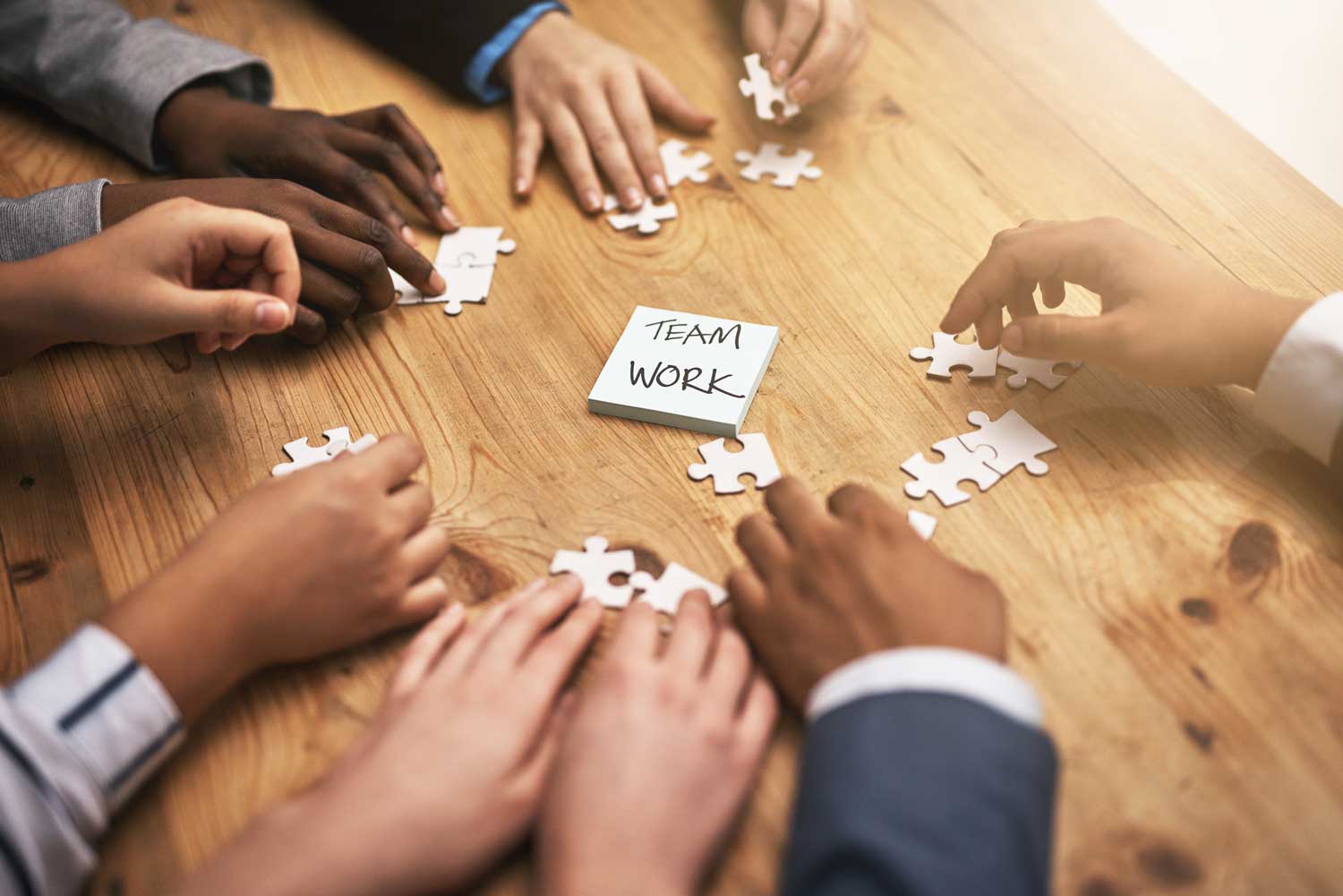 Hands cooperating to solve a puzzle with a 'TEAM WORK' note at the center.