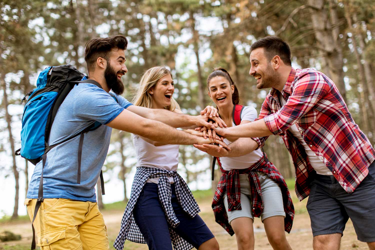 Joyful hikers with backpacks putting hands together in the forest.